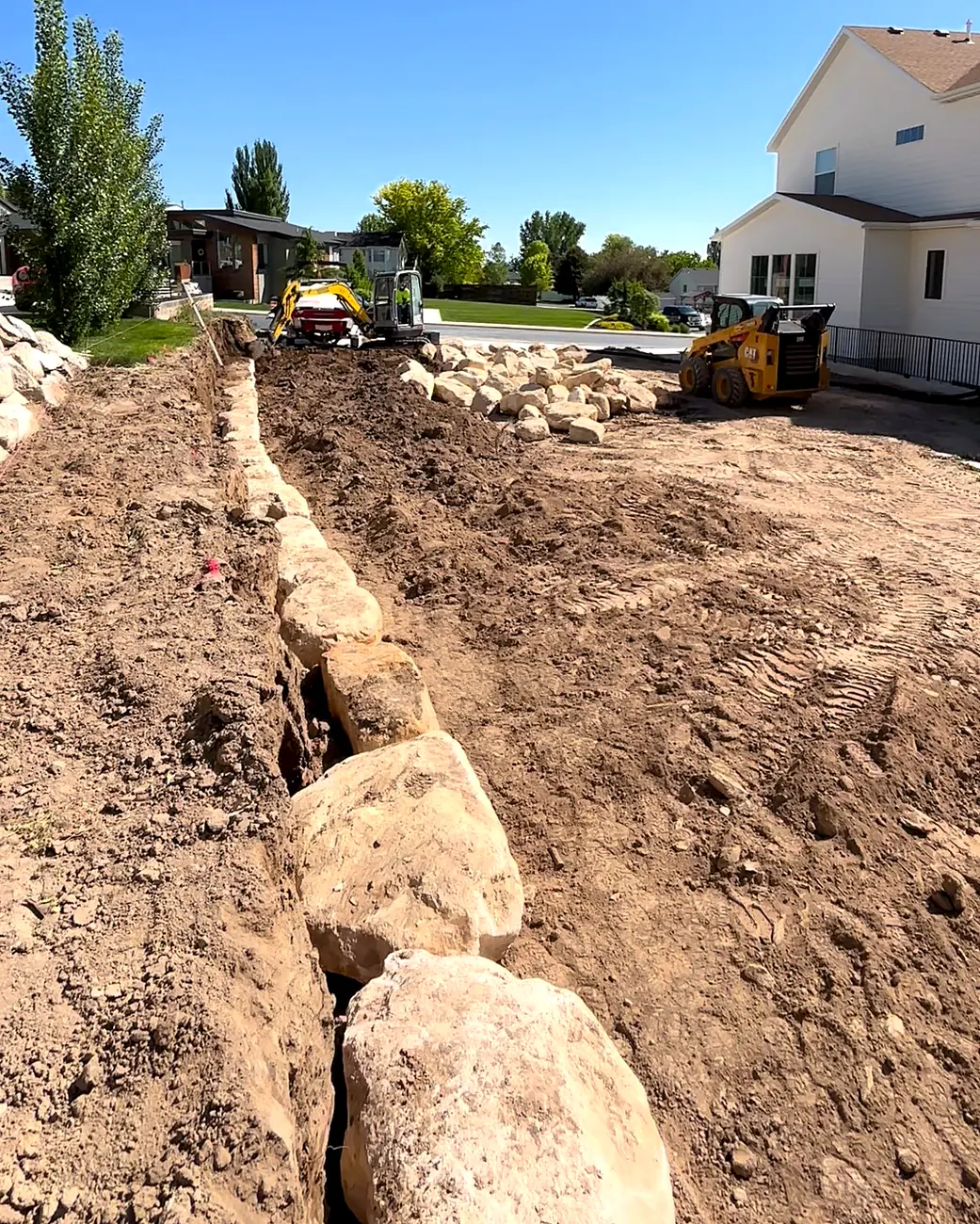 Row of boulders set along a trench in a backyard, with equipment behind