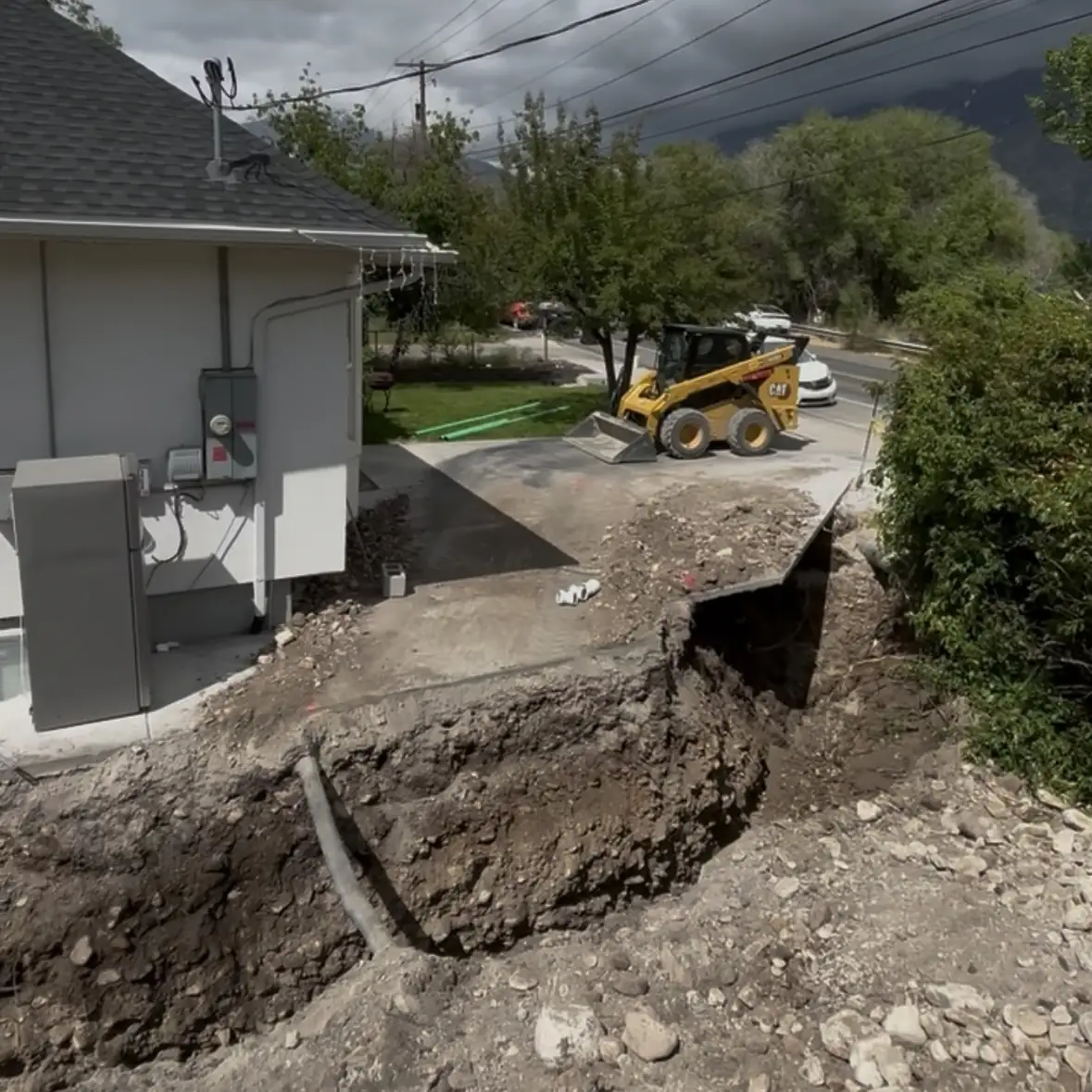 Deep excavation beside a house with a skid steer in the driveway