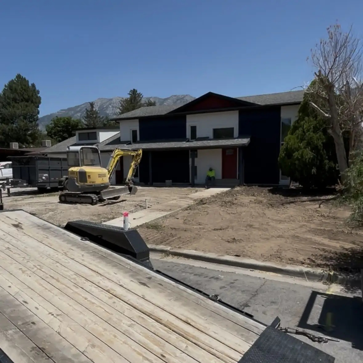 Mini excavator grading the bare front yard of a newer two-story home