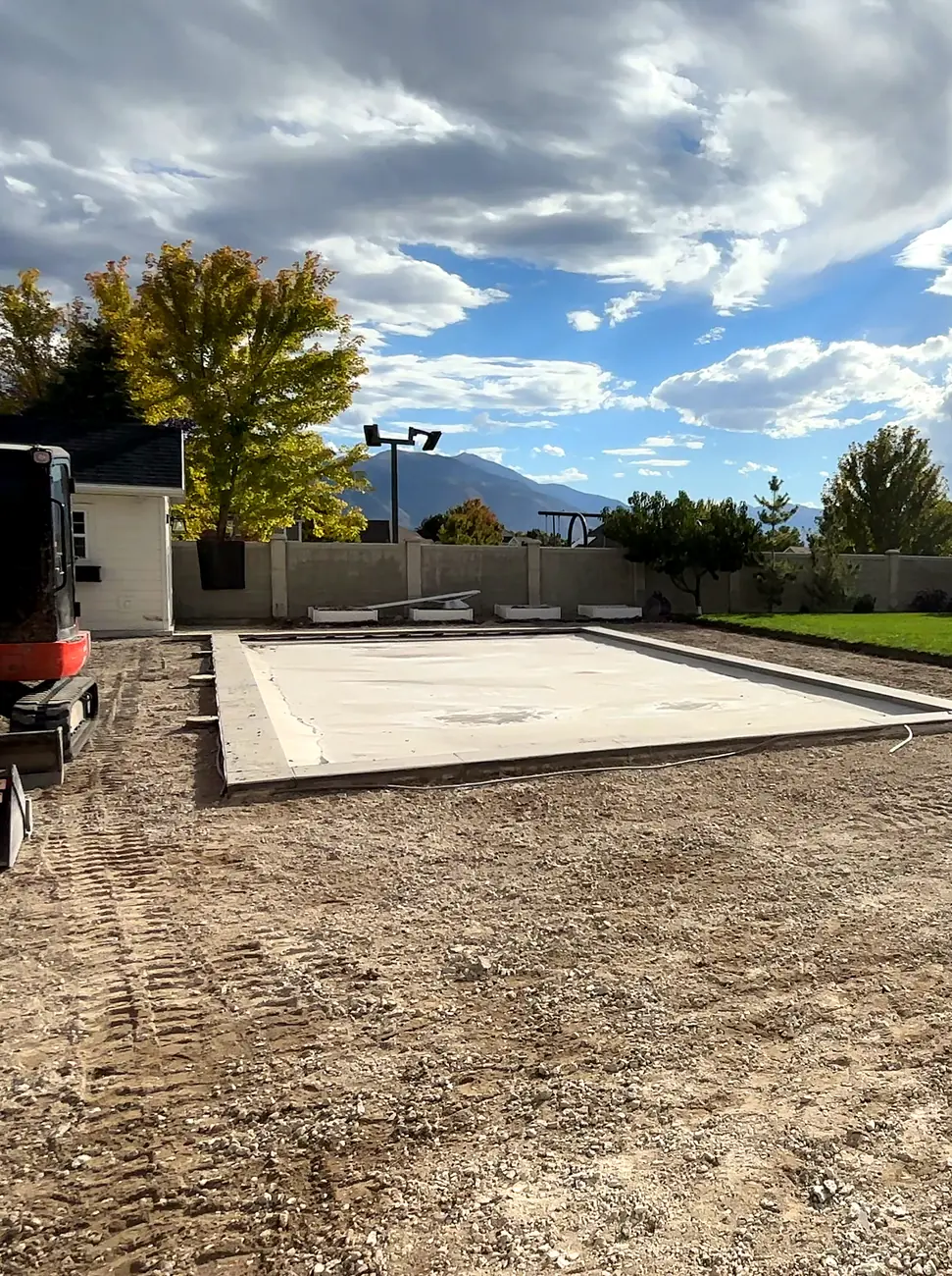 Same backyard with the concrete pool deck removed down to dirt, and a track loader beside the pool