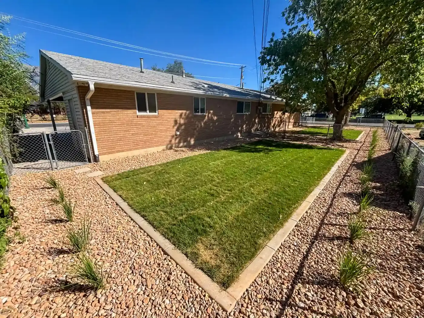 Side yard with a small lawn framed by rock and drought-tolerant grasses